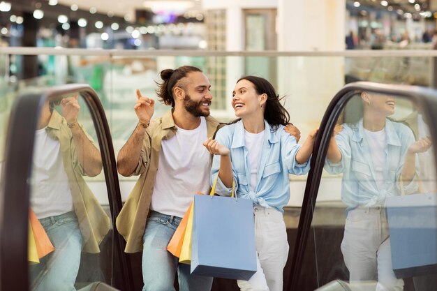 Rindo feliz, jovem casal europeu viciado em compras com sacolas se abraçando, divirta-se, aproveite as compras