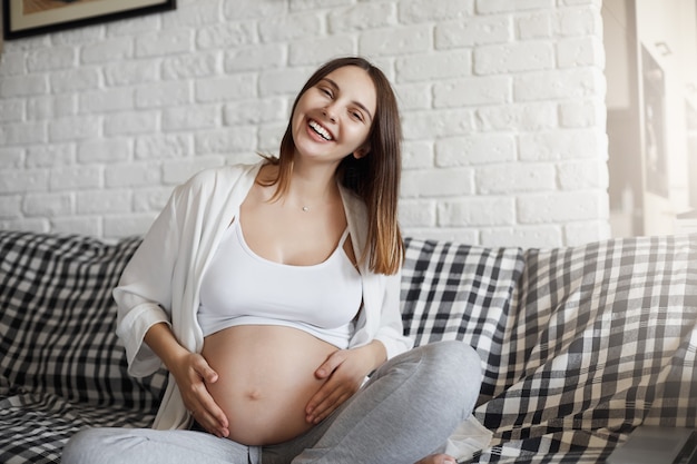 Foto rindo, jovem mãe desfrutando de seu bebê chutando e girando, segurando a barriga. primavera de uma nova vida. conceito de gravidez.