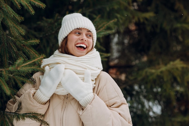Rindo jovem mulher retrato vestido casaco lenço chapéu e luvas gosta do tempo de inverno no parque de inverno com pinheiros