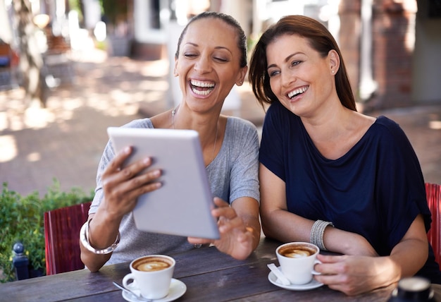 Rindo junto com a mídia social duas mulheres jovens olhando para um tablet em uma cafeteria