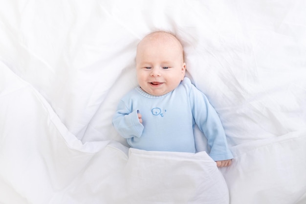 Rindo menino na cama debaixo do cobertor bebê sono saudável