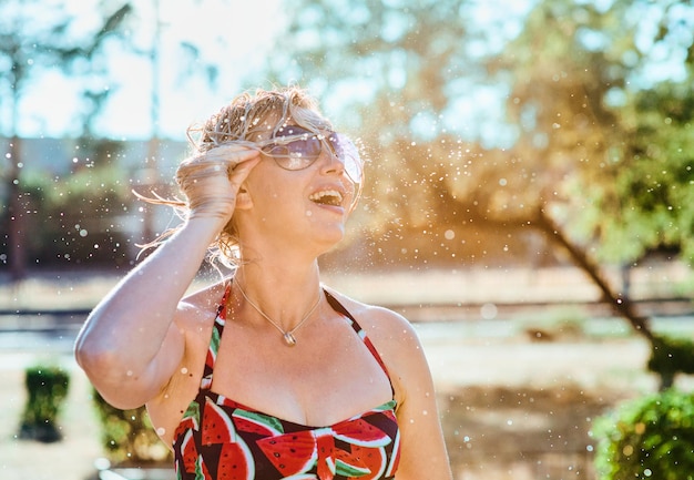 Foto rindo mulher loira emocional com cabelo molhado fazendo salpicos de água. férias, felicidade, diversão