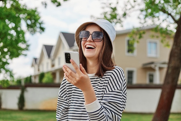 Rindo mulher positiva posando na rua da cidade com smartphone no fundo rindo com expressão feliz usando telefone celular para fazer selfie