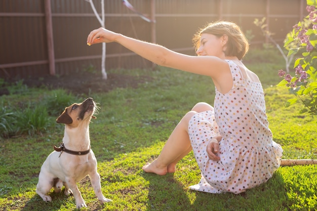 Rindo positiva, jovem de vestido brinca com seu amado cachorro inquieto sentado no quintal de uma