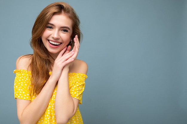 Rindo sorridente jovem linda loira escura com emoções sinceras, isoladas na parede de fundo com espaço de cópia, usando um vestido amarelo elegante de verão. Conceito positivo.