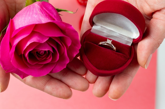 Ring in herzförmiger Schachtel und Blume in Händen. Valentinstag Geschenk