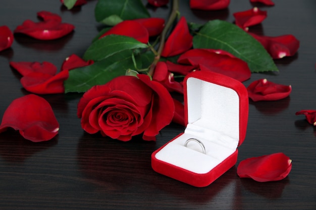 Ring umgeben von Rosen und Blütenblättern auf Holztisch Nahaufnahme