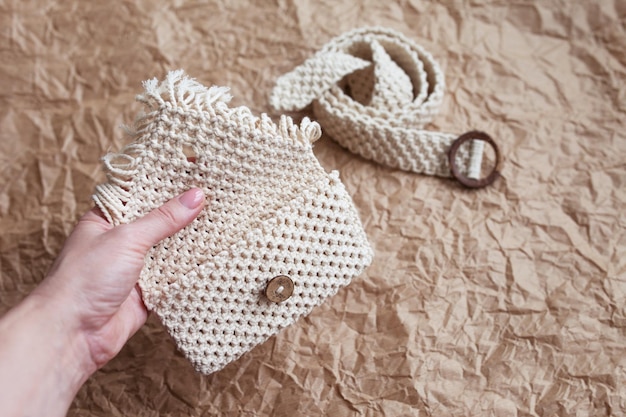 Riñonera de macramé hecha a mano sobre fondo de papel artesanal Riñonera de algodón macramé natural respetuosa con el medio ambiente Hobby tejer macramé hecho a mano Concepto moderno de verano