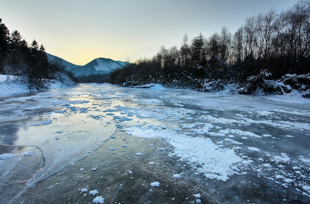 Rio Bela completamente congelado durante o frio extremo, sol da manhã refletido na camada de gelo coberta com manchas de neve. Liptovsky Hradok, Eslováquia