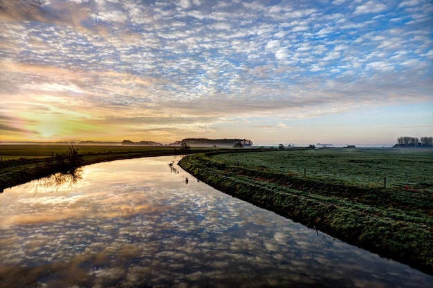 Un río con un cielo nublado y una granja al fondo.