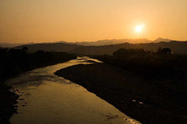 Río y cielo de la puesta del sol. Imagen de la silueta del río y de las montañas en el fondo de la tarde.