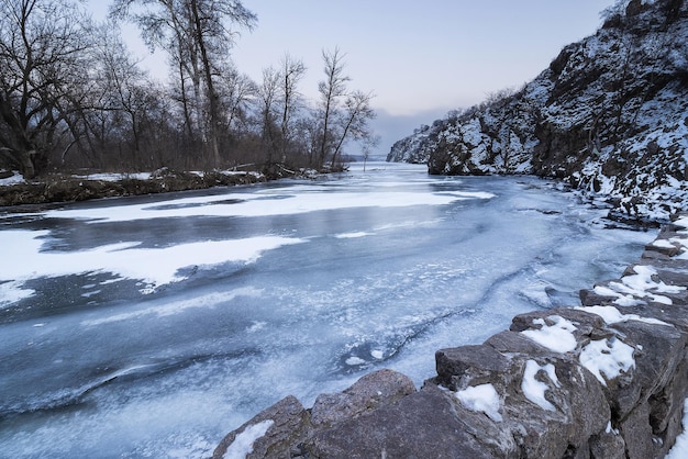 Rio coberto de gelo no inverno entre rochas e árvores