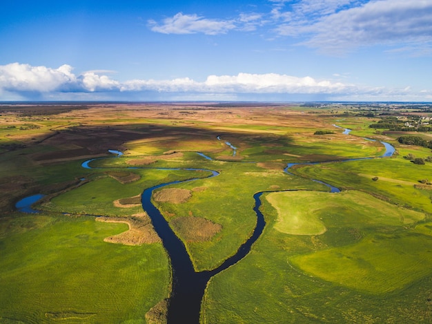 Un río corre a través de un campo verde con un cielo azul Foto aérea de Drone