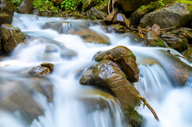 Rio de montanha com pequena cachoeira com águas cristalinas turquesa caindo entre pedregulhos molhados com espuma branca espessa.