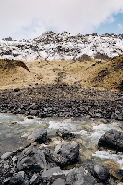 Rio de montanha no sopé da montanha com um pico coberto de neve de grama seca amarela nas montanhas