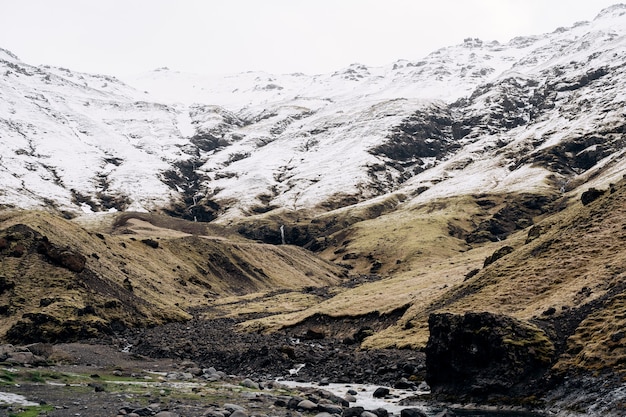 Rio de montanha no sopé da montanha com um pico coberto de neve de grama seca amarela nas montanhas