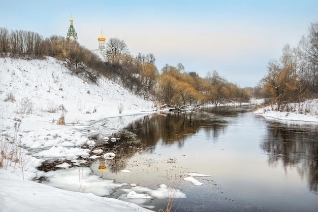 El río fluye entre la nieve invernal y el templo con la cúpula dorada en la orilla alta