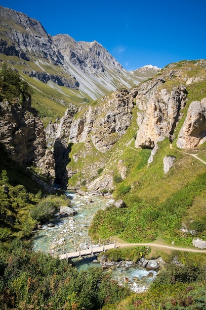 Río de montaña y puente de madera en los Alpes franceses del valle del Parque Nacional de Vanoise