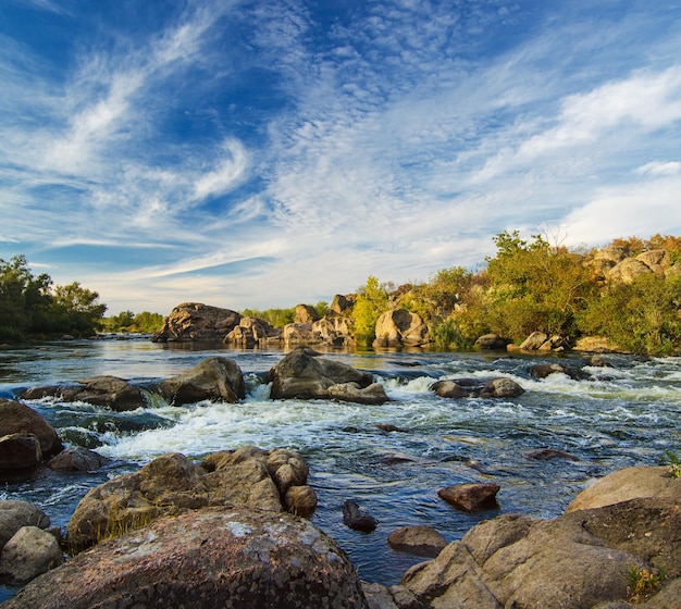 Río de montaña que fluye rápido corriente de agua en las rocas con cielo azul