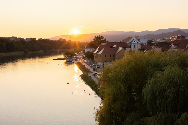 Río que fluye con casas antiguas en maribor al atardecer