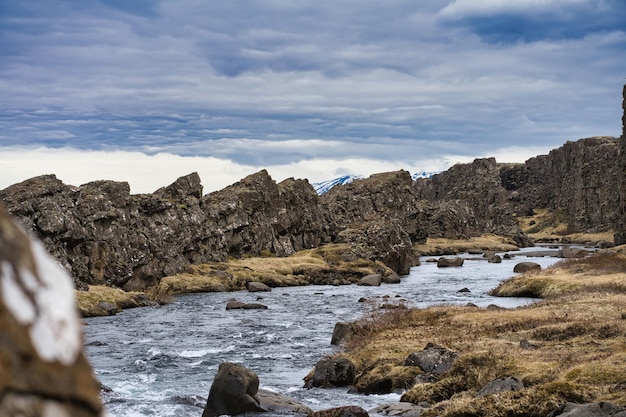 Río rocoso al lado de la montaña con altas montañas rocosas en el fondo