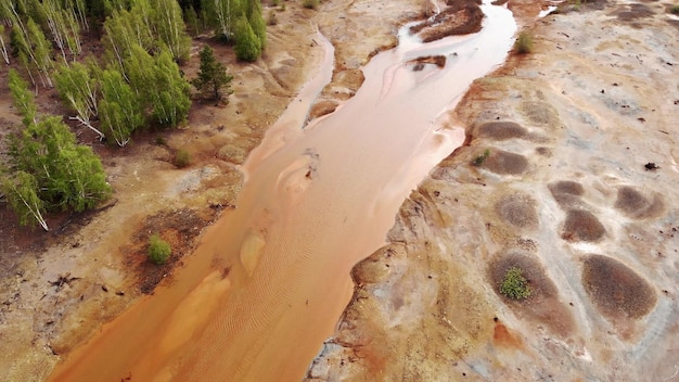 Rio tóxico laranja sem vida perto de árvores verdes Planta industrial polui solo e floresta Vista aérea drone voando