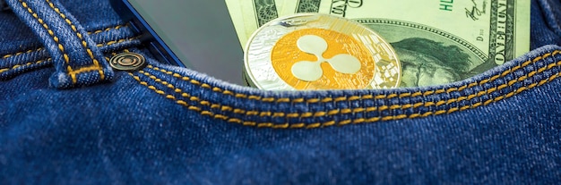 Ripple Coin Kryptowährung Bannerfoto, Kryptomünze in der Tasche von Blue Jeans neben US-amerikanischem Geld