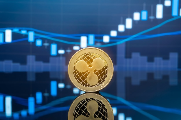 Ripple (XRP) y concepto de inversión en criptomonedas. Monedas de ondulación de metal físico con gráfico de precios de mercado de intercambio de comercio global en el fondo.