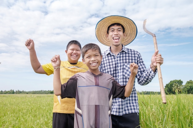 Rir feliz fazendeiro asiático homem e dois filhos sorriam e segurando ferramentas no campo de arroz verde