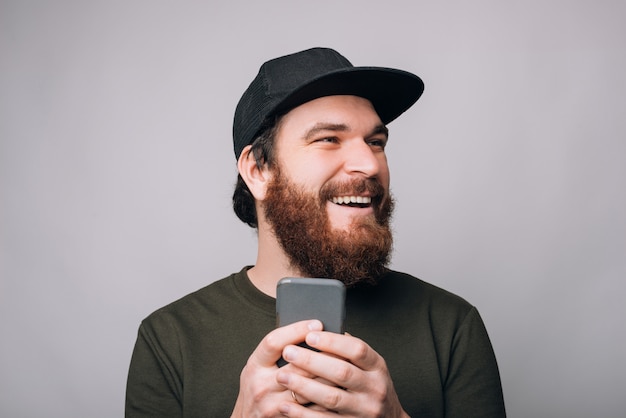 Rir homem barbudo está segurando seu telefone olhando de lado.