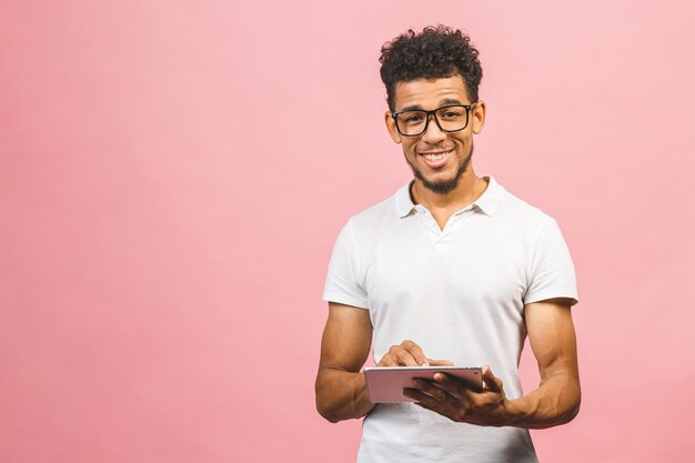 Rir jovem afro-americano masculino segurando um Touch Pad Tablet PC isolado contra o fundo rosa