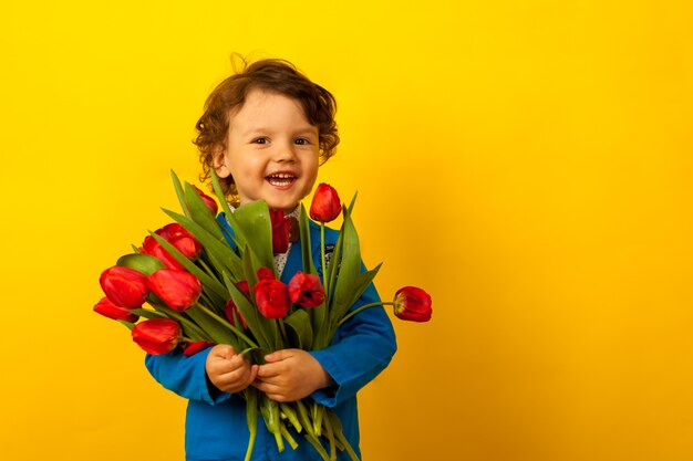 Rir menino com um buquê de tulipas vermelhas. Dia das Mães,