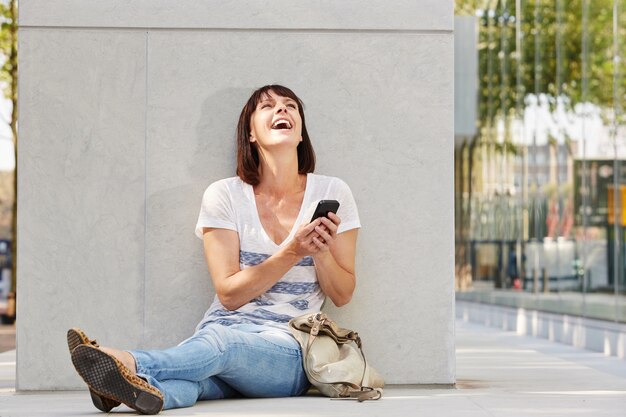 Rir mulher mais velha sentada no chão com bolsa e telefone