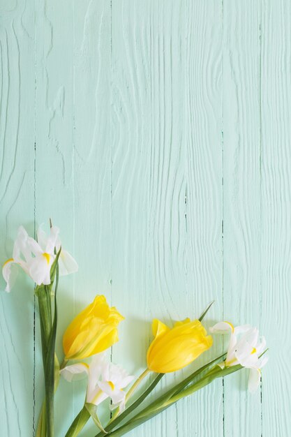 Íris brancas e tulipas amarelas na superfície verde de madeira