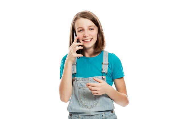 Risa adolescente en overol de mezclilla y una camiseta azul hablando por un teléfono inteligente. .