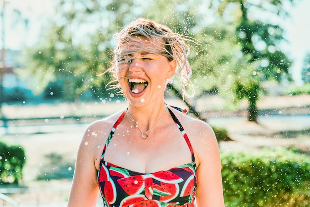 risa emocional mujer rubia con el pelo mojado haciendo salpicaduras de agua. Vacaciones, felicidad, diversión.