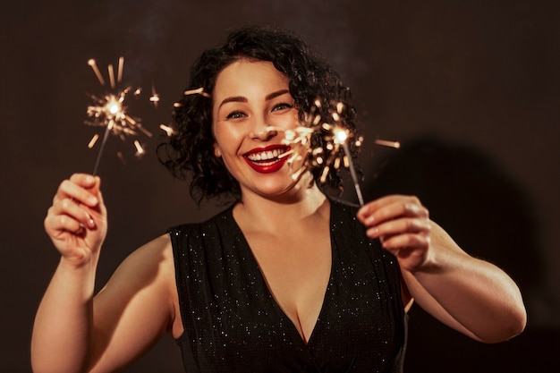 Risa a mujer joven con bengalas. Hermosa morena con labios rojos y cabello rizado con un vestido de fiesta. Fiestas y eventos. Año Nuevo y Navidad.