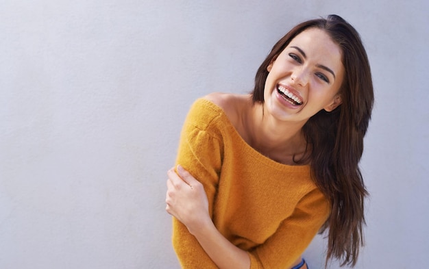 Las risas son divertidas Retrato de una hermosa joven riendo mientras está de pie contra una pared gris