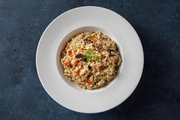 Foto risoto, arroz italiano com cogumelos, legumes e salsa servido em prato de porcelana branca