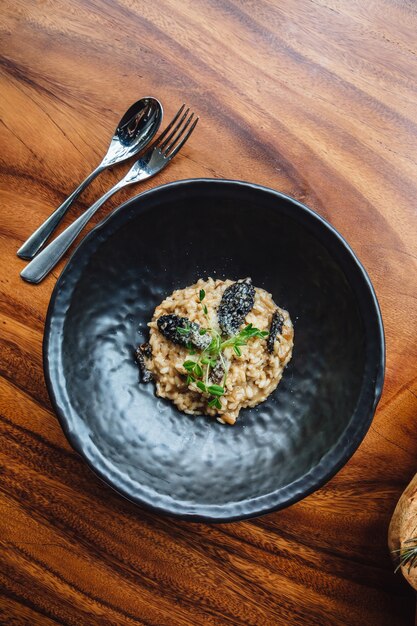 Risoto com cogumelo, erva fresca e queijo parmesão na placa preta na tabela de madeira.