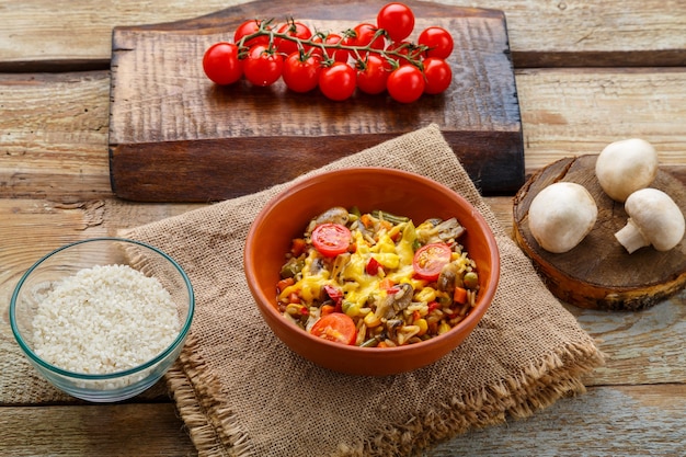 Risoto com cogumelos em um prato sobre um fundo de madeira em um guardanapo de linho ao lado de tomates.