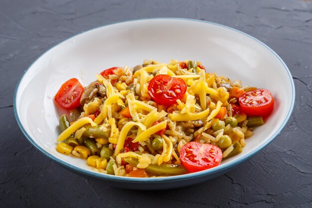 Risoto com cogumelos, queijo e legumes em um prato sobre um fundo cinza. Foto horizontal