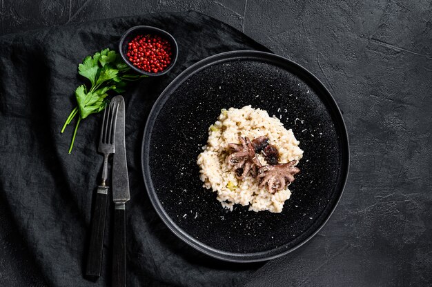 Risoto com polvo e cogumelos, salsa e especiarias. Fundo preto. Vista do topo. Espaço para texto