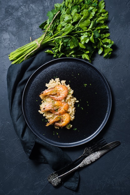 Risoto italiano com camarão em uma placa preta, um grupo do coentro.