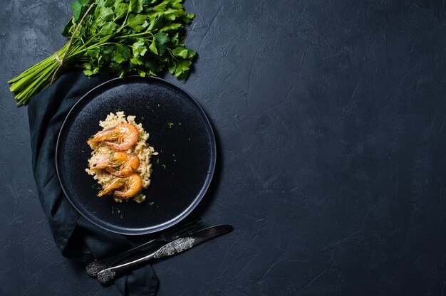 Risoto italiano com camarão em uma placa preta, um grupo do coentro.