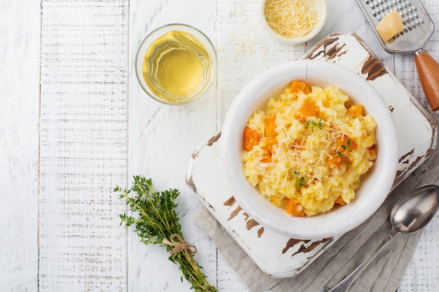 Risotto de calabaza con tomillo, ajo, queso parmesano y vino blanco sobre superficie de madera clara. Enfoque selectivo. Estilo rústico. Vista superior.