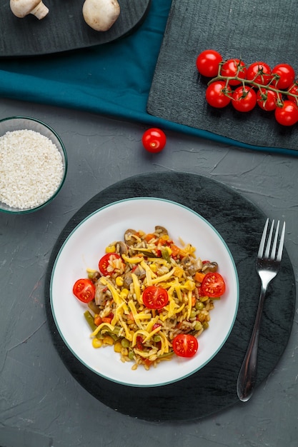 Risotto con champiñones en un plato sobre un fondo gris cerca de los ingredientes en posavasos negros. Foto vertical