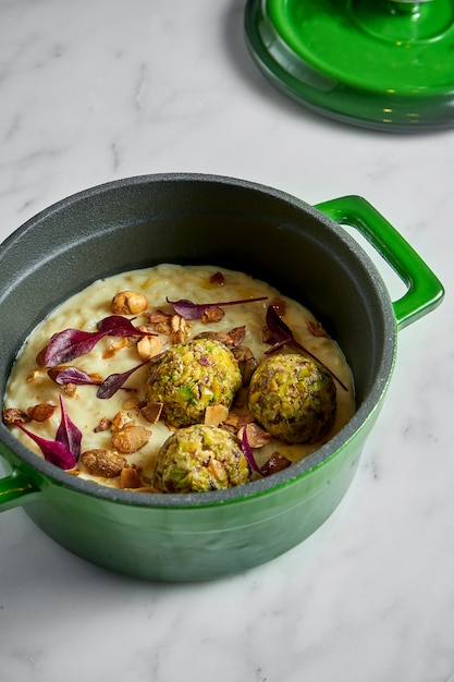 Risotto cremoso con bolas de apio, maní y hojas de albahaca en una olla verde sobre mármol blanco