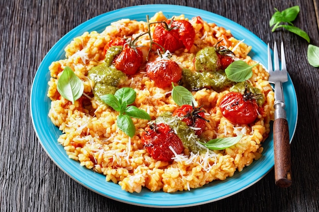 Risotto cremoso de tomate con tomates cherry y pesto de salsa en un primer plano de placa azul