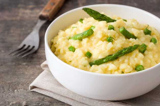 Risotto con espárragos, perejil y guisantes en un recipiente sobre una mesa de madera rústica